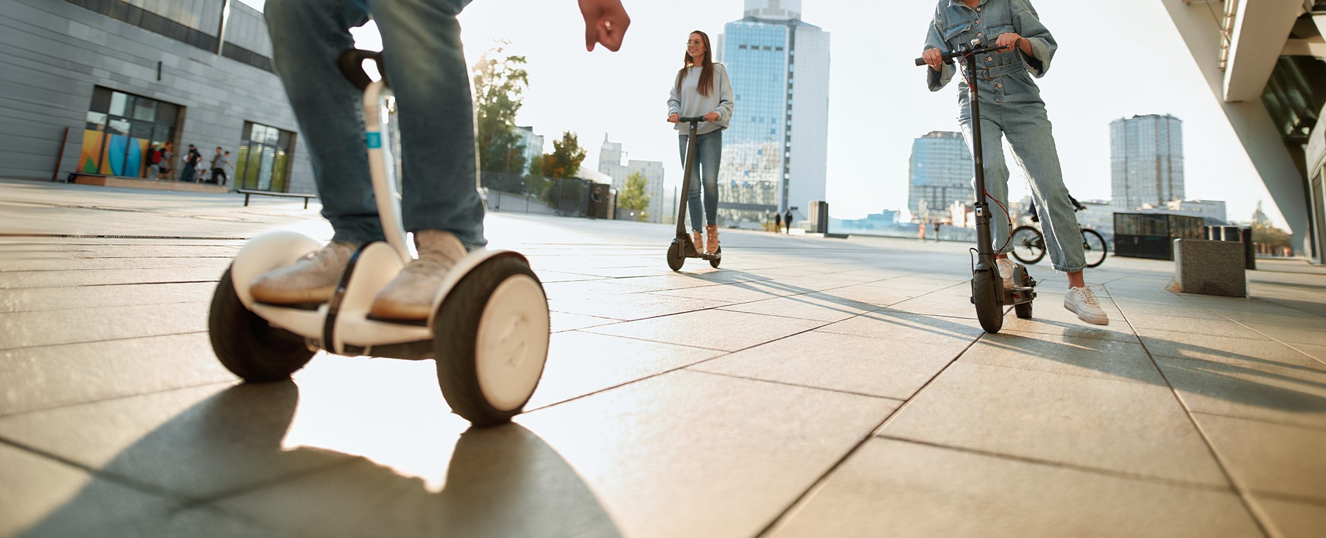 Jazdci na elektrických kolobežkách a jazdec na segwayi nachádzajúci sa v meste pri východe slnka.