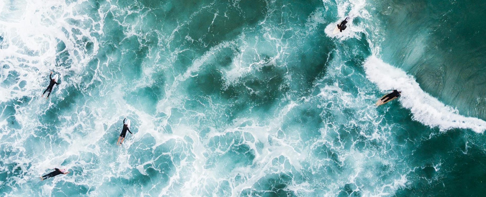 Pohľad z výšky na viaceré osoby plávajúce na surfoch v morských vlnách.